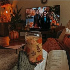 a person is holding an open book in front of a television with pumpkins on it