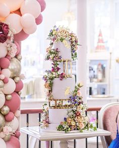 a three tiered cake sitting on top of a table next to balloons and flowers