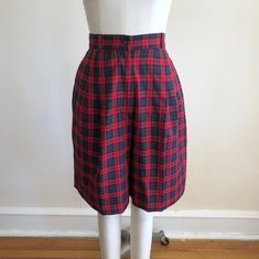 "Red and black/navy pleated plaid shorts from the 1990s. High-rise fit. Shorts measure 14.5\" (37 cm) flat across waist and 24.5\" (62 cm) flat across hip. The inseam is 9\" (23 cm) and the rise is 13.5\" (34 cm). The length of the shorts is 21\" (53.5 cm). Original size is a 10. Rayon/polyester blend." Classic Plaid Cotton Bottoms, Fitted Plaid Shorts, Fitted Knee-length Plaid Bottoms, Plaid High-waisted Fitted Shorts, Fitted Plaid High-waisted Shorts, Plaid High Waist Cotton Shorts, High-waisted Plaid Bottoms With Built-in Shorts, Fitted Plaid Cotton Shorts, Red Plaid Shorts