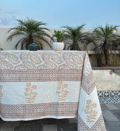 a table covered with a white and brown cloth next to potted plants on a patio