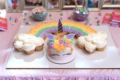 cupcakes and cakes on a table with a rainbow in the background