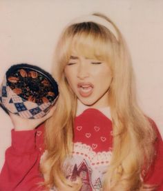 a woman with long blonde hair holding a bowl of food in front of her face