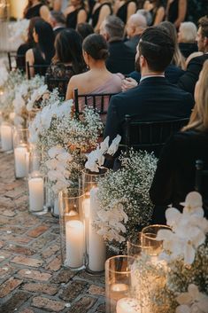 an outdoor ceremony with candles and flowers in vases on the aisle, surrounded by people