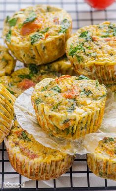 several muffins on a cooling rack with tomatoes and herbs in the top one