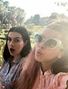 three young women sitting next to each other in front of trees and bushes with their mouths open