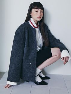 a woman sitting on the floor wearing a coat and skirt