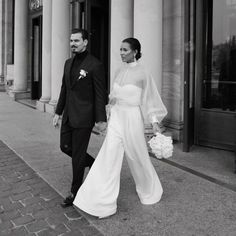 a bride and groom walking down the street together in front of a building with columns