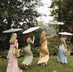 four women in dresses are holding umbrellas over their heads while walking through the grass