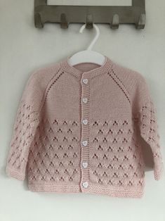 a pink knitted sweater hanging on a clothes hanger next to a white wall