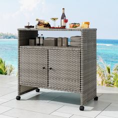 a wicker bar with bottles and glasses on it next to the ocean or beach