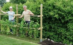 two people standing next to each other in a garden filled with green plants and vegetables