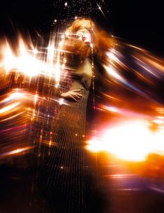 a woman standing in the middle of a street at night with bright lights behind her