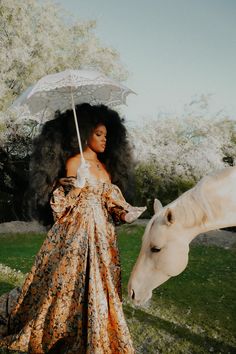 a woman standing next to a white horse on top of a lush green field holding an umbrella