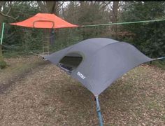 a tent is pitched up in the woods with an orange tarp attached to it