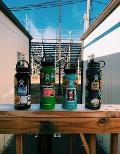 three water bottles sitting on top of a wooden table next to a white building and power lines