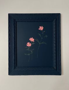 two pink flowers in a blue frame on the wall