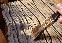 a person holding a paintbrush over a piece of wood