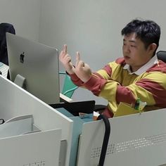 a man sitting in front of a laptop computer on top of a desk next to another person