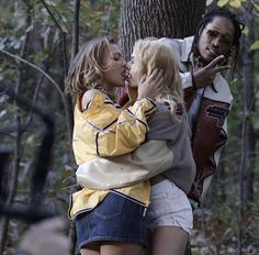 three people standing in front of a tree with one person kissing the other's cheek