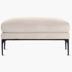 an upholstered footstool with black legs and a light colored fabric cover