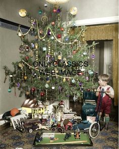 a young boy standing in front of a christmas tree with toys on the floor next to it