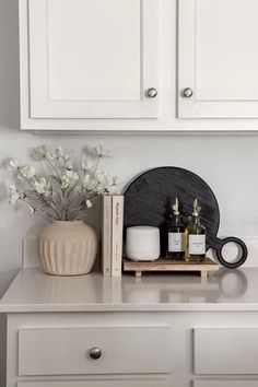 a white dresser with some bottles and candles on it's shelf next to a vase filled with flowers