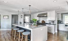 a large kitchen with white cabinets and counter tops, along with bar stools that match the hardwood flooring