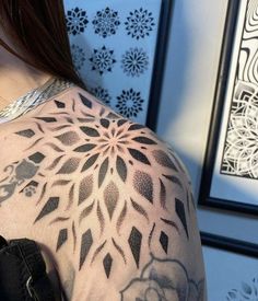 a woman with a tattoo on her back and shoulder is standing in front of a wall