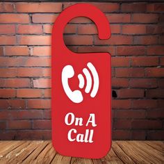 a red sign that says on a call with a phone in the middle, against a brick wall