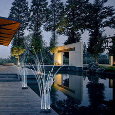 a water fountain in the middle of a wooden walkway next to a lake at night