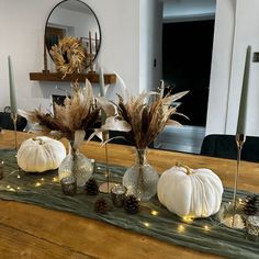 the table is decorated with white pumpkins and dried grass in vases on it