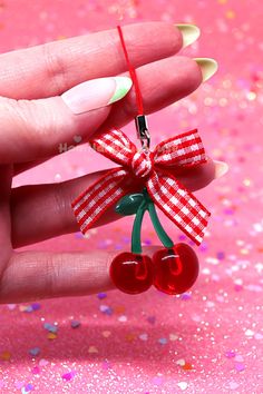 a hand holding a cherry ornament with a bow