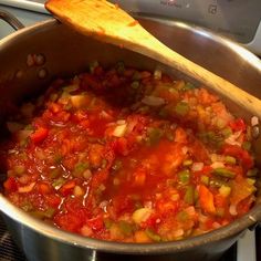 a pot filled with lots of food sitting on top of a stove next to a wooden spoon