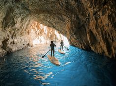 two people are paddling in the water with their paddles under a large cave