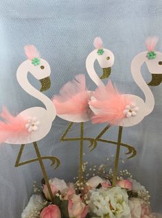 three flamingos are standing on top of a cake with pink flowers and greenery