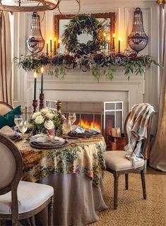 a dining room table set for two with candles and flowers on the fireplace mantel