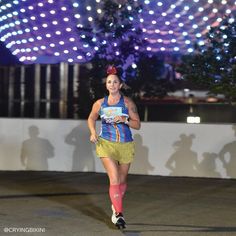 a woman running at night in front of a ferris wheel with lights on the background