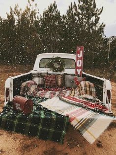 an old pickup truck is covered in plaid blankets and christmas decorations with a joy sign on the back