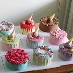 there are many cakes on the table with icing and toppings in different colors