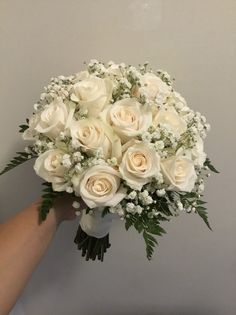 a bouquet of white roses and greenery in someone's hand