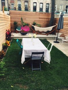 a table and chairs are set up in the back yard with hammocks on the fence