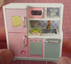 a hand holding a small toy kitchen with pink and green accents on the door,