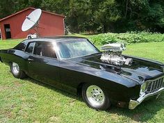 an old black car parked on top of a grass covered field next to a red barn