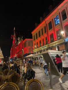 many people are walking around in the city at night, with red lights on buildings behind them