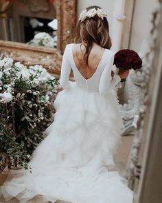 a woman in a white wedding dress holding a bouquet and looking at herself in the mirror