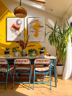 a dining table with four chairs and two potted plants on the wall behind it