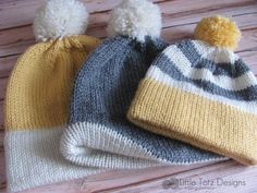 two knitted hats sitting on top of a wooden table next to each other with pom poms