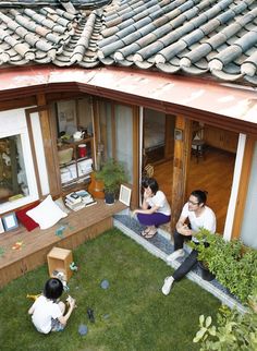 two people sitting on the grass in front of a house with an open door and windows