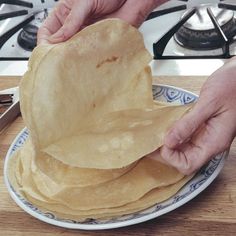 two hands holding tortillas on a plate