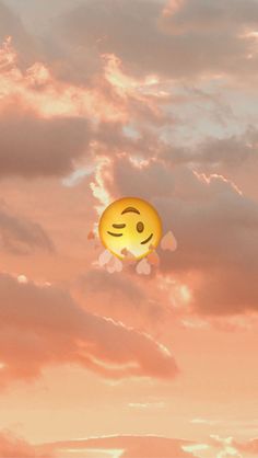 a yellow smiley face floating in the air with clouds and sky behind it at sunset